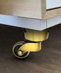 Attached vintage zinc alloy swivel caster with brass bronze finish under furniture, 1-3/4 inch OD wheel. Product: Vintage Zinc Alloy Swivel Casters 2 Pack, 1-3/4 Inch OD, Antique Brass Bronze Finish, Universal Furniture Casters For Beds, Cabinets, Chairs, Sofas, Tables, Desks, And More.