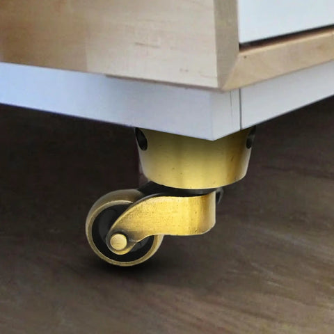 Attached vintage zinc alloy swivel caster with brass bronze finish under furniture, 1-3/4 inch OD wheel. Product: Vintage Zinc Alloy Swivel Casters 2 Pack, 1-3/4 Inch OD, Antique Brass Bronze Finish, Universal Furniture Casters For Beds, Cabinets, Chairs, Sofas, Tables, Desks, And More.