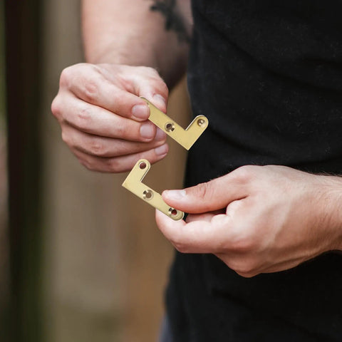 Hands holding two gold 360 Degree Rotating Pivot Hinge Set For Concealed And Secret Doors with mounting holes.