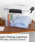 3 Pack 19 Quart Waterproof Storage Bins IP68 Clear Plastic Totes With Gasket Sealed Lids on a table with books and blankets inside.