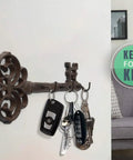 Brown Cast Iron Skeleton Key Wall Hook With Three Heavy Duty Coat Holders For Classic Farmhouse Vibes And Simple Down Home Entryway Organization Built Rock Solid For Everyday Hanging with keys attached.