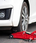 Front Wheel Replacement For Two And A Half Inch Iron Wheel For Two Ton Hydraulic Floor Jacks Heavy Duty Pro Grade Universal Roller Accessory With Professional Bearing For Horizontal Jack And RV Stabilization, shown installed on a red hydraulic jack under a car.