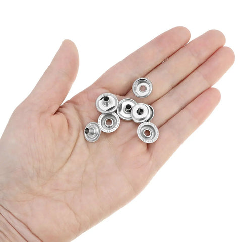 Hand holding stainless steel snap fasteners from the 200-Piece Stainless Steel Snap Fastener Kit, 15mm Snap Caps, for DIY repairs.