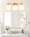 Next Level Three Light Bathroom Vanity Lights In Brushed Gold Finish With Milky White Glass Globe Shades Modern Wall Sconce Over Mirror above a stylish bathroom vanity with floral accents.