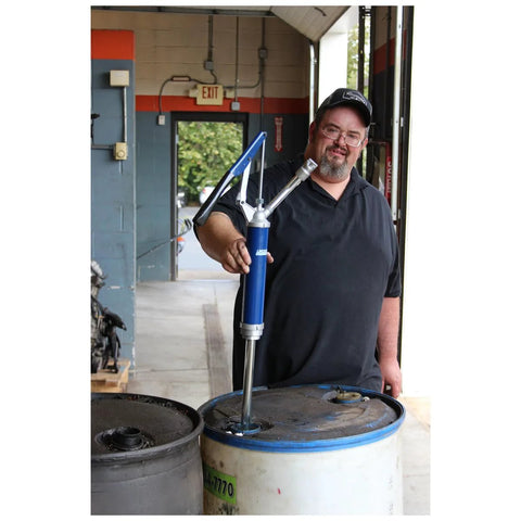Man using Lincoln 1340 Lever Action Barrel Pump for industrial lubrication, attached to a large blue drum in a workshop.