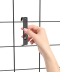 Hand placing black utility hanger on grid wall panel, part of 15 Pack Gridwall Notch Hooks Black Utility Hangers for Grid Wall Panels Pegboard Display