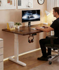 Smooth Riding Electric Height Adjusting Standing Desk With Touch Memory Presets And Heavy Duty Anti Collision Technology Created As A Reliable Gaming Computer Table For Hassle Free Home Office Setups Around Twenty Eight By Fifty Five Inches features a man working at a solid wood desk.