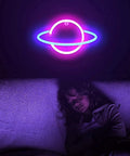 Planet Neon Sign USB Powered Saturn LED Light With Easy On Off Switch Aesthetic Wall Decor For Bedroom And Gaming Room Hanging Neon Night Light Featuring Blue And Pink LEDs glowing above a sleeping child on a couch