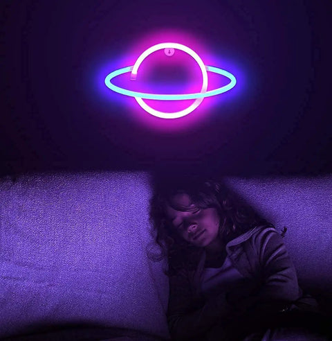Planet Neon Sign USB Powered Saturn LED Light With Easy On Off Switch Aesthetic Wall Decor For Bedroom And Gaming Room Hanging Neon Night Light Featuring Blue And Pink LEDs glowing above a sleeping child on a couch