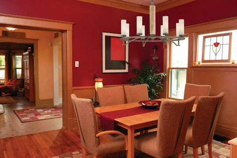 Dining room with modern chandelier, wooden table, and red accent wall, showcasing cozy ambiance and stylish decor.