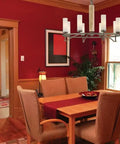 Dining room with chandelier, wooden table and chairs with red walls, showcasing indoor lighting setup.