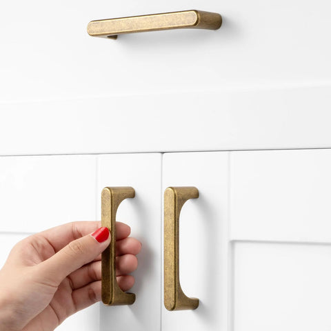 Hand holding 10 Pack Antique Brass Drawer Pulls 3 Inch Vintage Cabinet Handles on white cabinet doors