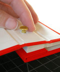 Hand inserting a brass screw post into a scrapbook page, showcasing the 20 Pack Of Chicago Screw Posts With 10mm Brass Plated Finish Ideal For Scrapbooking Photo Album Binding And Leather Craft Repair Giving Solid Stability Serving As A Legit Game Changer For Serious Diy Hobbyist Workstations.