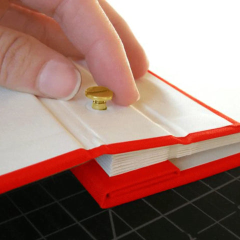 Hand inserting a brass screw post into a scrapbook page, showcasing the 20 Pack Of Chicago Screw Posts With 10mm Brass Plated Finish Ideal For Scrapbooking Photo Album Binding And Leather Craft Repair Giving Solid Stability Serving As A Legit Game Changer For Serious Diy Hobbyist Workstations.