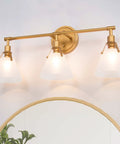 Three Light Gold Vanity Light Fixtures With White Frosted Glass Shades Over Mirror In Brushed Antique Gold Finish, Modern Bathroom Vanity