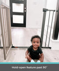 Baby sitting by an extra wide auto close baby gate with hold open for busy homes kid friendly safety gate for families pressure mounted