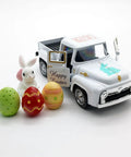 White truck with bunny and color eggs on vintage farmhouse tabletop; Metal Truck Decor With Mini Rabbits And Color Eggs