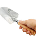 Hand holding Built To Last Stainless Steel Garden Shovel With Ergonomic Wooden Handle For Digging, Planting, Lawn Care And Trowel Tasks.