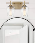 Dope Octave Bohemian Clear Glass Vanity Wall Light Two Light Bath Fixture In Warm Brass installed over round mirror