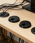 Premium Desktop Grommet Covers Slick Cable Organizers Hella Tough ABS Plastic Wire Routing Kit For Working From Home Office Setup No Mess Cord Management 5 Pack Black, with cables routed through 2.5 inch openings.