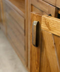 Side view of Six Pack 5 Inch Antique Brass Cup Pulls With Distinctive Layered Ribbed Multi Sectioned Design on a wooden cabinet