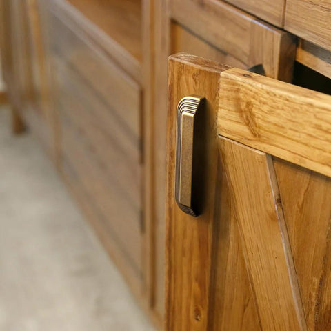 Side view of Six Pack 5 Inch Antique Brass Cup Pulls With Distinctive Layered Ribbed Multi Sectioned Design on a wooden cabinet