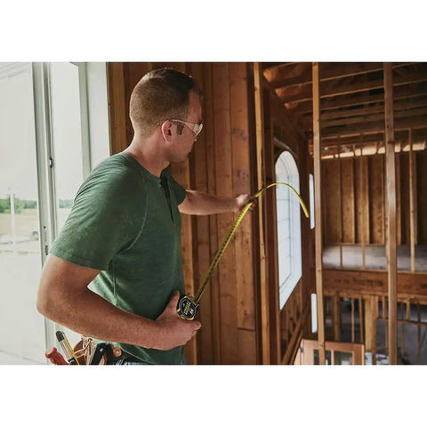 Person using FatMax Auto Lock Tape Measure 25 Ft With 1-1/4 Inch Wide Blade Detachable End Hook in a wooden construction area