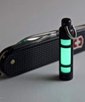 Embrite Glow Fob With Green Embrite Pellet, Aircraft-Grade Aluminum Keychain Accessory next to Swiss Army knife