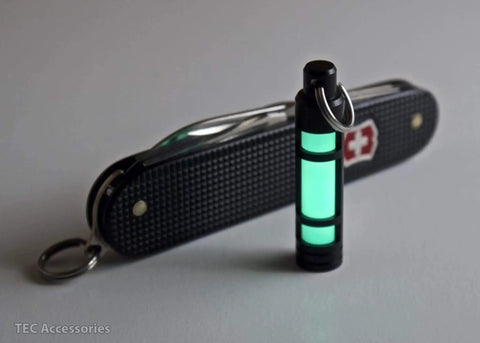 Embrite Glow Fob With Green Embrite Pellet, Aircraft-Grade Aluminum Keychain Accessory next to Swiss Army knife