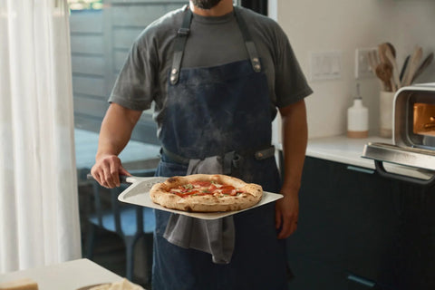 Ooni 12-inch aluminum pizza peel with handle carrying a pizza in a home kitchen.