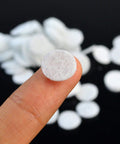 Close-up of a single 10 mm microdermabrasion cotton filter on a fingertip, part of 200 Pcs Microdermabrasion Cotton Filters Replacement 10 mm Universal Fit Diamond Dermabrasion Vacuum Filters for Suction Machines Soft Skin Friendly Sponge Filters for Home Spa Facial Care White.