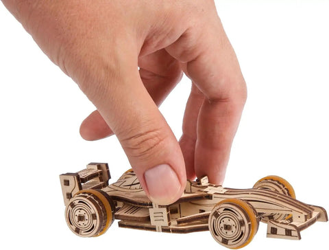 Compact Racer 3D Puzzle Kit With 90 Pieces Snap Together No Glue Required Wood Model Five Point Two Inch Brown Buildable Educational Toy For Kids And Adults STEM Gift And Hobbyist Favorite, hand holding assembled wooden race car