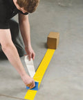 Heavy Duty Polyester Floor Marking Tape In Bright Yellow With Kick Ass Adhesion For Concrete Warehouses and 2 Inch By 100 Foot Roll being applied to a concrete floor.