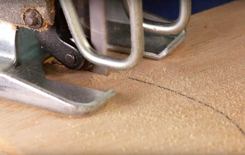 Jigsaw cutting wood; silver metal base plate and blade area visible with pencil line