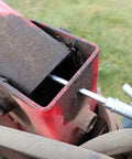 LockNLube recessed fitting adapter; silver metal nozzle inserted into red housing on dusty outdoor machinery.