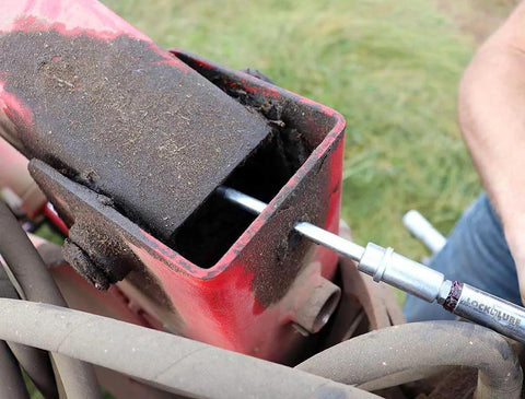 LockNLube recessed fitting adapter; silver metal nozzle inserted into red housing on dusty outdoor machinery.