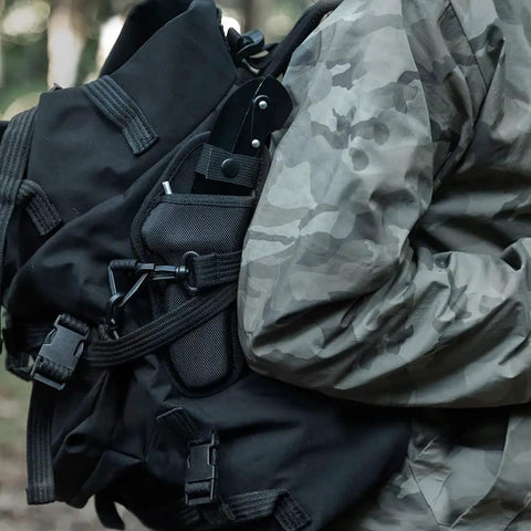 Person carrying backpack with all-black sharp edge folding sickle with wooden handle, portable grass cutter visible.