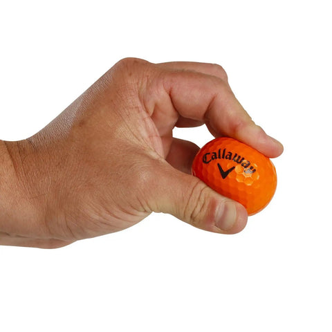 Hand holding an orange foam golf ball with HEX dimples, featuring the brand logo. Soft Flight Foam Practice Golf Balls 9 Pack Orange With HEX Dimples For Indoor And Outdoor Practice Safe Durable Balls To Sharpen Your Short Game And Swing.