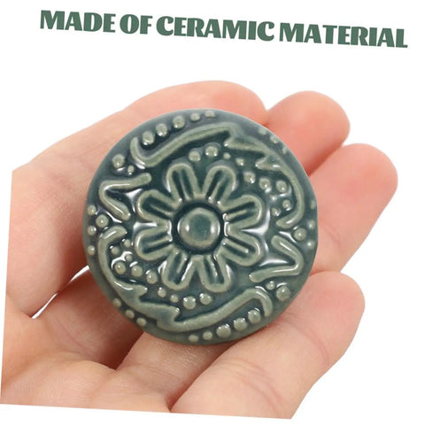 Hand holding a single knob from Set Of 10 Ceramic Drawer Pulls And Kitchen Cupboard Knobs With Vintage Pattern Single Hole Cabinet Door Handles For Dresser And Closet Hardware In Celadon Blue