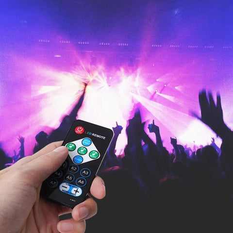 Hand holding remote for Black Light UV Disco Ball LED Party Light 6W Sound Activated with glowing purple stage lights in background