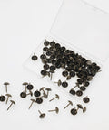 Top Notch Antique Brass Upholstery Tacks For Furniture 100 Pack decorative nail heads in a clear container with scattered tacks.