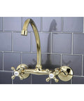 Gold wall mounted kitchen faucet with cross handles on a gray tiled backsplash