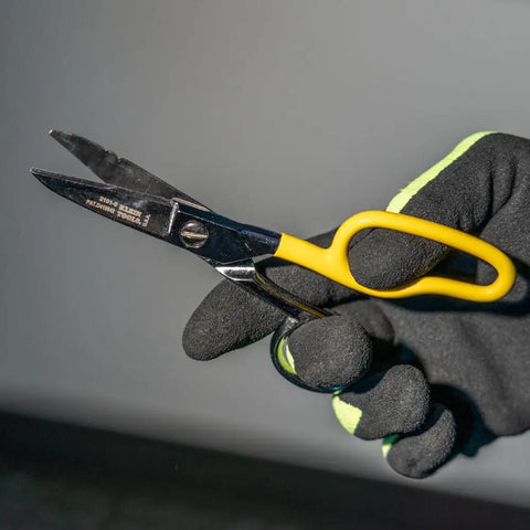 Black-gloved hand holding yellow-handled snip from Cable Splicer Kit With Electricians Knife And Free Fall Snip Includes Leather Tool Holder For Belts Up To Two Inches The Essential Gear For Cable And Phone Techs On The Job.