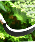 Close-up of a Two Pack Manganese Steel Weeding Sickle Garden Tool Set blade against green foliage.