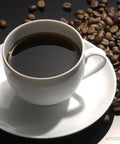 Cup of black coffee surrounded by coffee beans on a glossy surface
