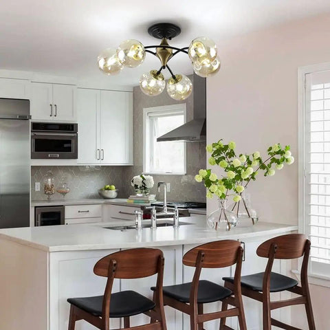 Modern kitchen with Bold Black Chandelier Lighting With Glass Orbs above a white island, featuring wooden chairs.
