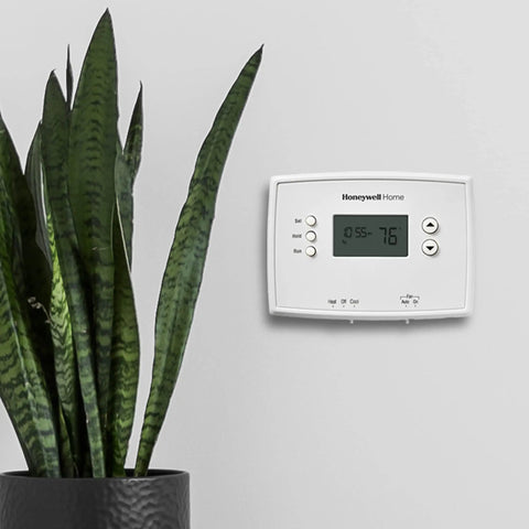 Programmable Thermostat With One Week Programming And Digital Display White mounted on wall next to plant