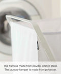 Close-up of foldable laundry basket with steel frame and polyester bag, shown near a washing machine. Focus on the frame.