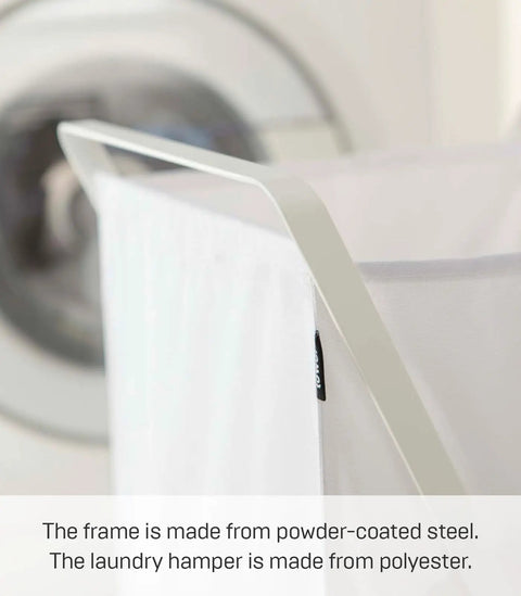 Close-up of foldable laundry basket with steel frame and polyester bag, shown near a washing machine. Focus on the frame.