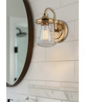 Bathroom wall fixture with a brass finish and clear glass shade near mirror